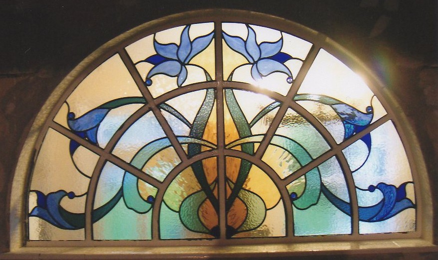 A sweeping design within an arched window with blue Art Nouveau flowers.